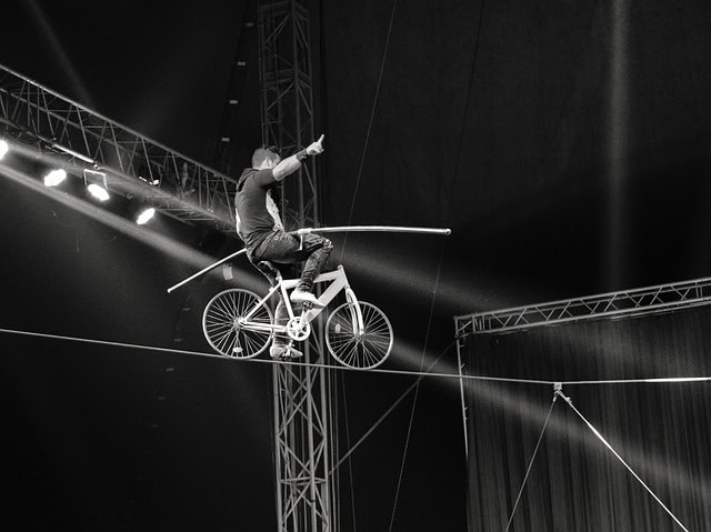 Circus performer balancing on a bicycle on a tightrope during a show.